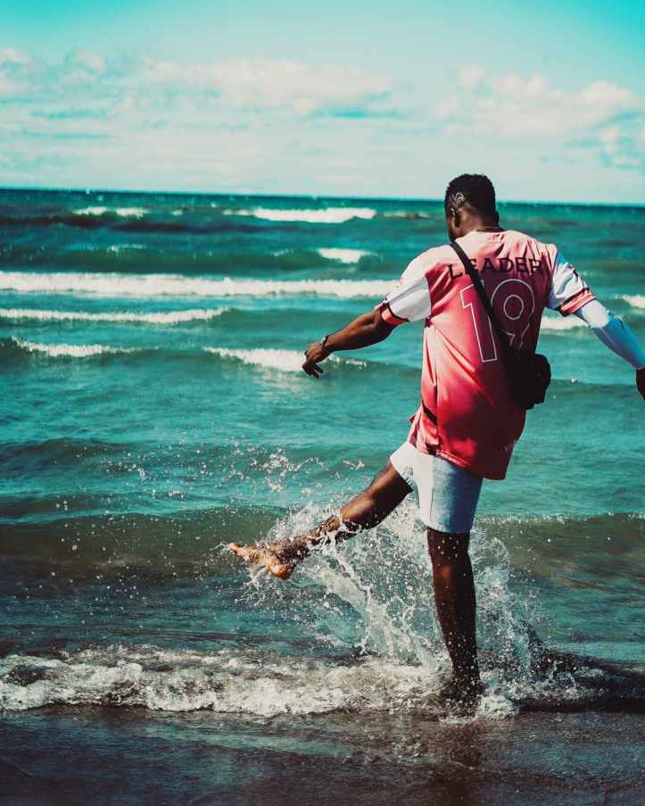 back view photo of man kicking water by the beach
